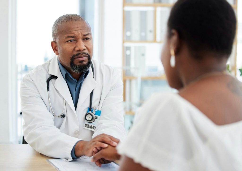 Serious gp in a consult with a patient. African american doctor talking to a patient in a checkup.